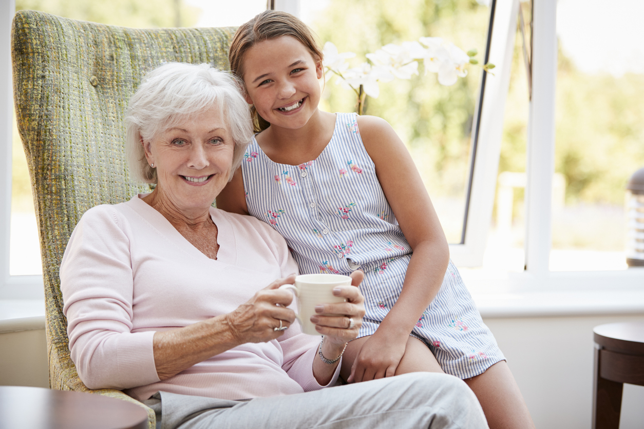 Portrait Of Granddaughter Visiting Grandmother In Lounge Of Retirement Home